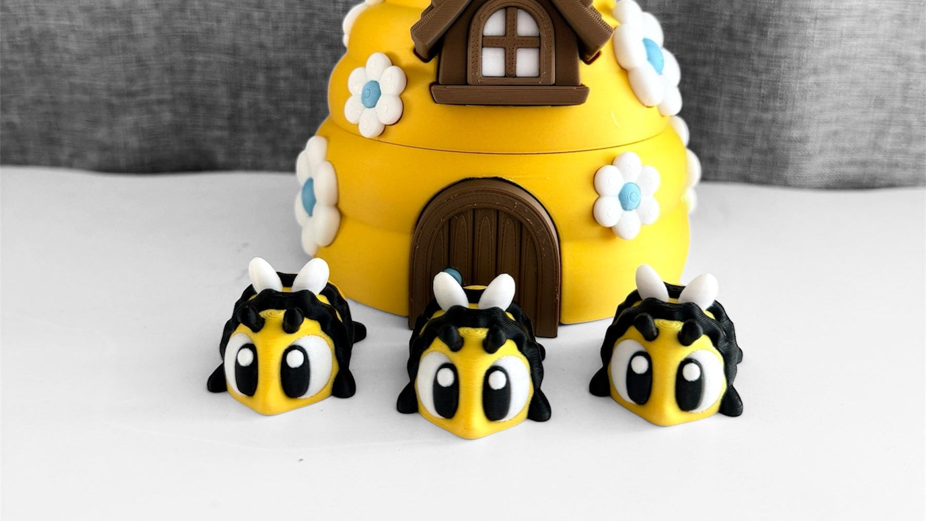 Yellow bee hive with three bee figures on a white surface and gray background